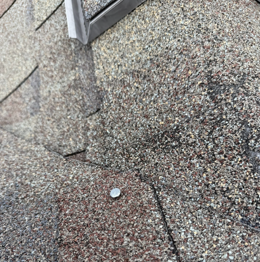 Close-up of an exposed roofing nail and a cracked shingle found during a roof inspection in Superior, WI.