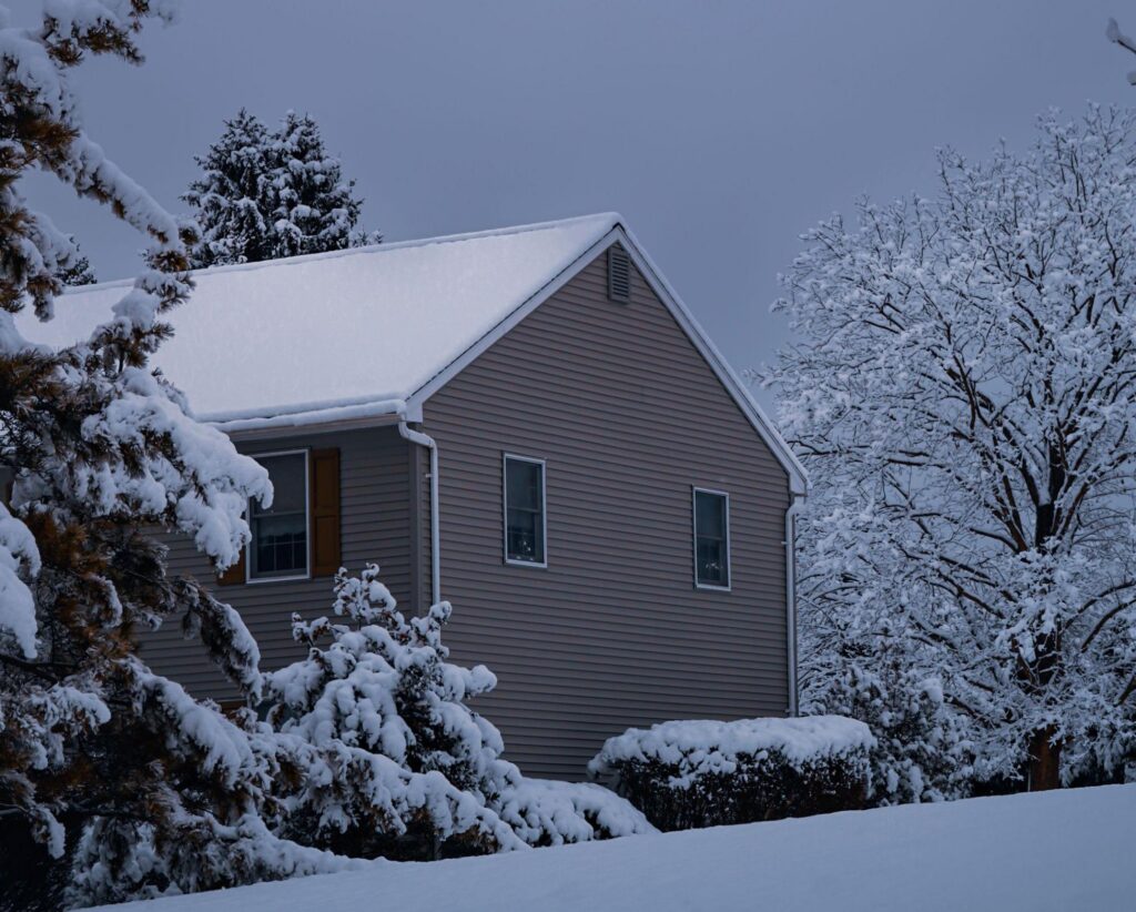 Fresh snow covering the roof of a two-story home, limiting winter shingle sealing